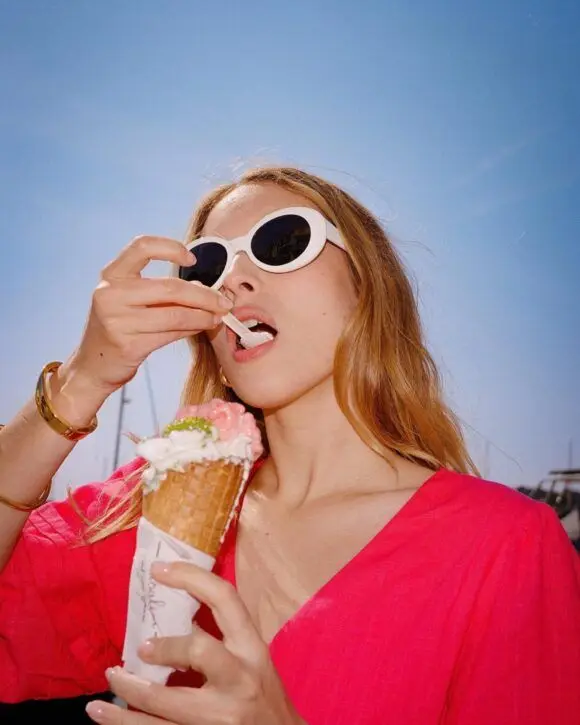 Woman in white oval sunglasses eating pink waffle ice cream cone