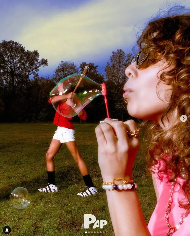 Editorial portrait: woman blowing oversized iridescent soap bubble in park