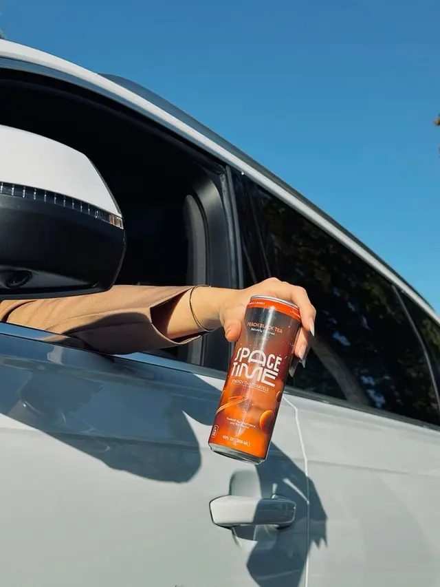 Hand Holding 'Space Time' Peach Black Tea Can Out of White Car Window