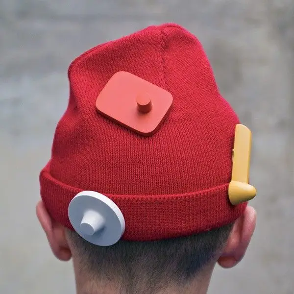 Red knit beanie with three geometric sculptural pins (coral square, white disc, mustard sl