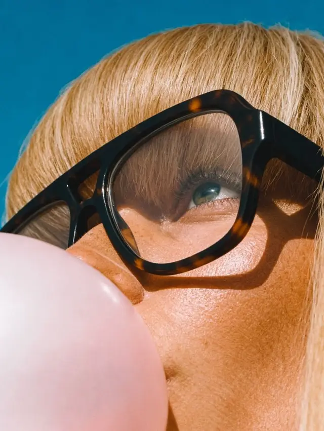 Close-up portrait with tortoiseshell glasses blowing pink bubble gum