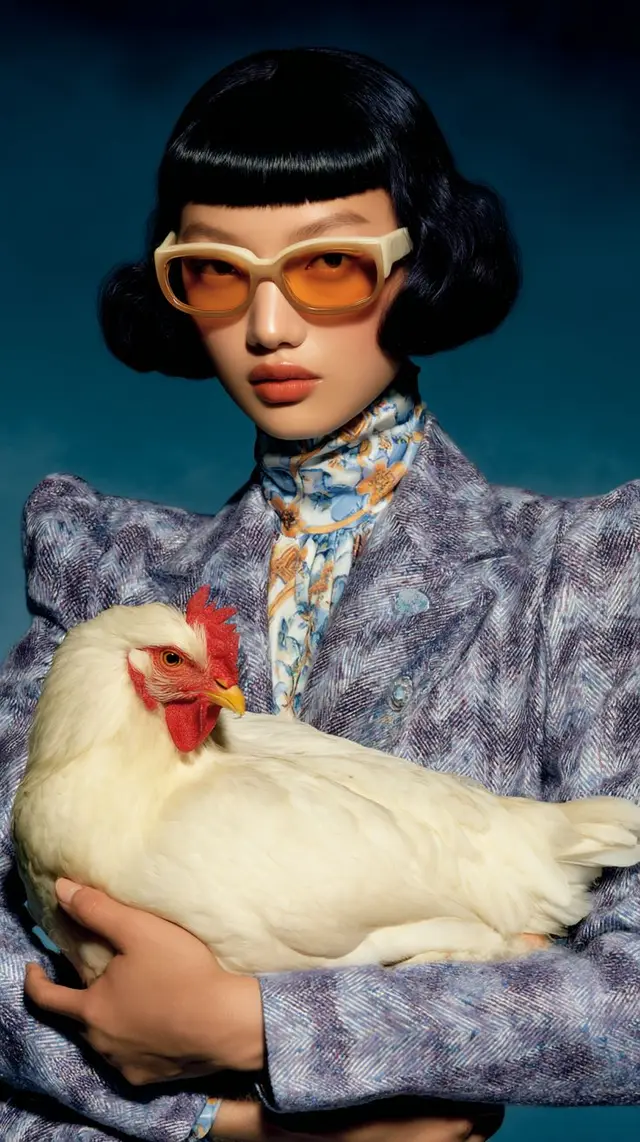 Editorial portrait — model in cream acetate sunglasses cradling a white hen