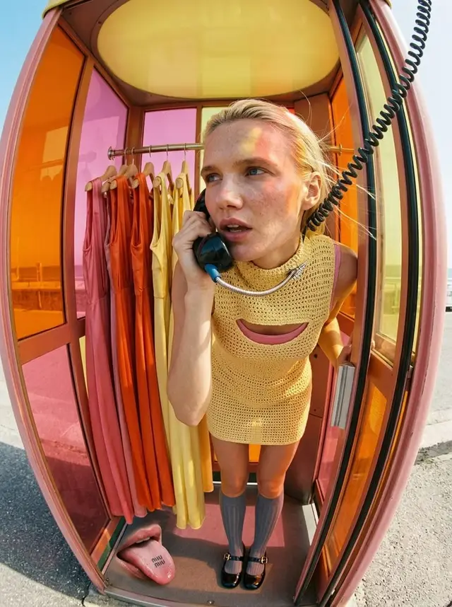 Retro fashion editorial: model in yellow crochet mini dress inside orange-pink phone booth