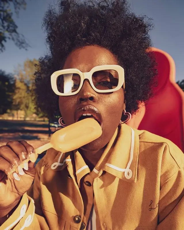 Golden-hour editorial portrait with oversized white sunglasses and orange popsicle