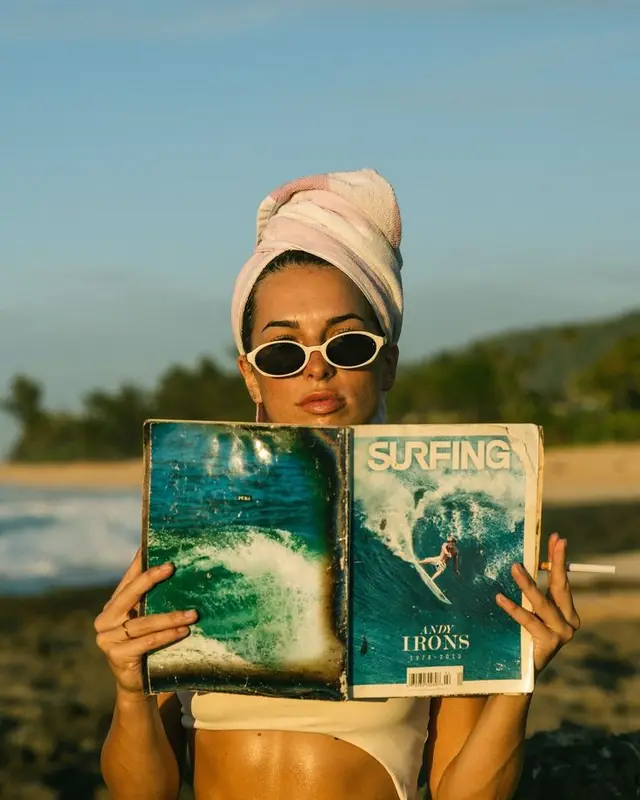 Woman with towel turban and cat-eye sunglasses holding 'SURFING' magazine (Andy Irons on
