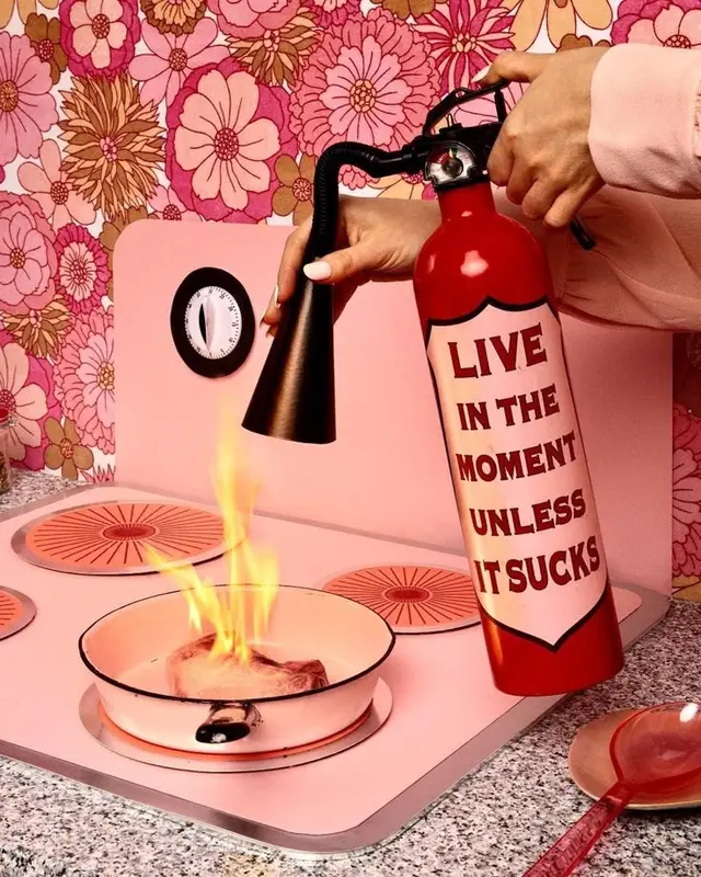 Novelty fire extinguisher in pink 1970s-style kitchen with flaming pan