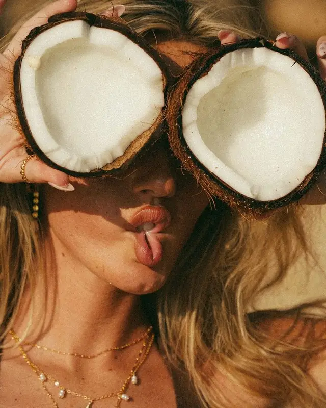 Sunlit portrait — woman holding halved coconuts over eyes