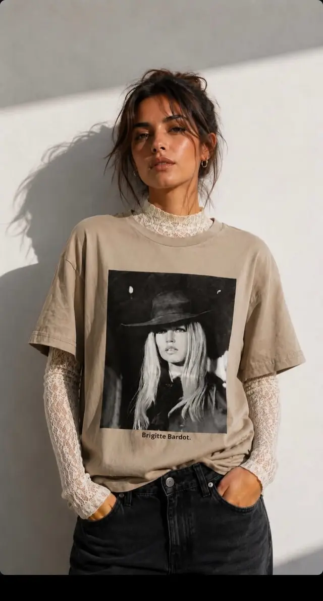 Beige Brigitte Bardot graphic tee layered over white lace top with black high‑waist jeans