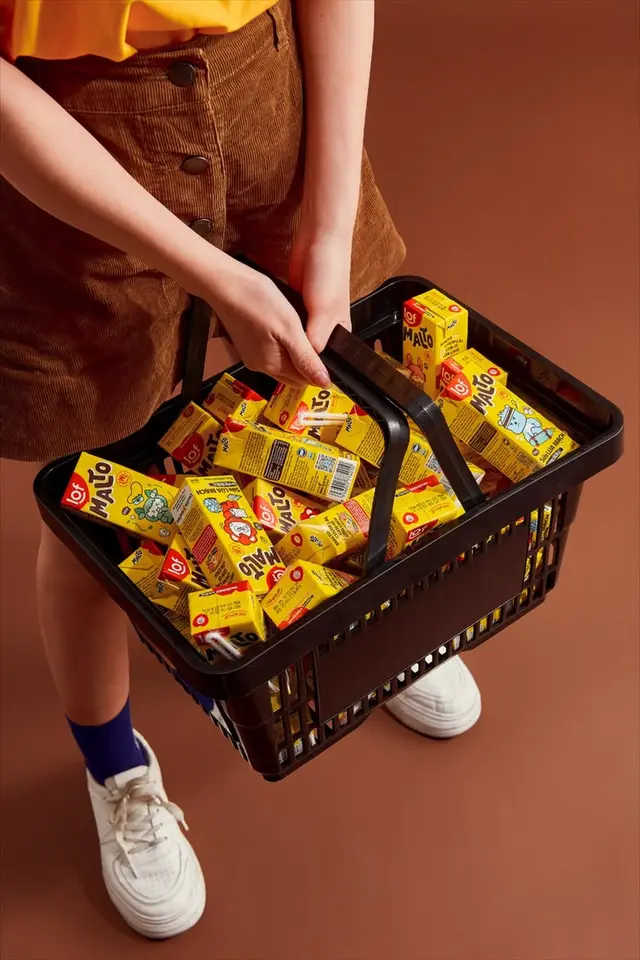 Black shopping basket overflowing with yellow 'MALTO' beverage cartons