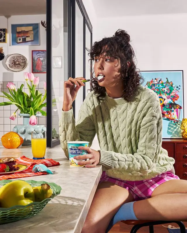 Woman eating yogurt at marble kitchen island in cable-knit sweater