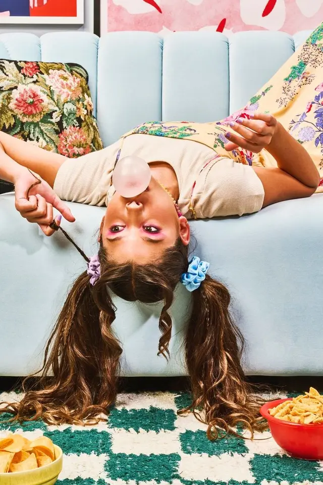 Girl blowing bubble gum upside-down on pastel sofa