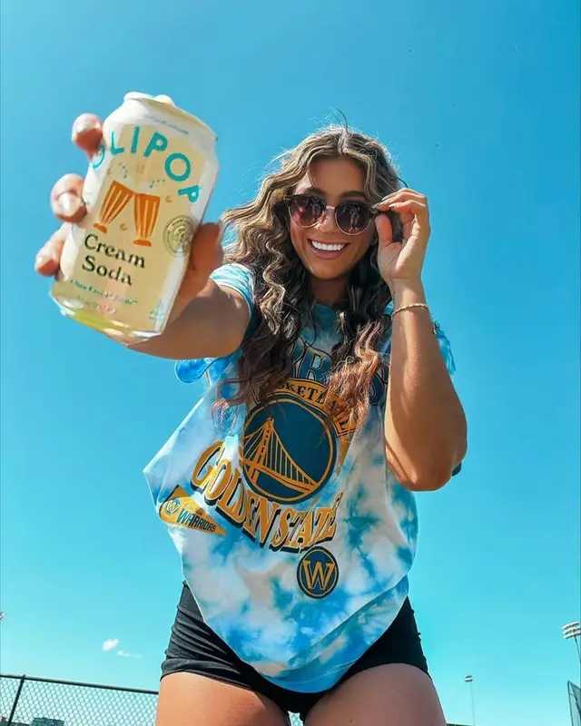 Smiling woman holds a can of cream soda wearing Golden State Warriors tie-dye tee against