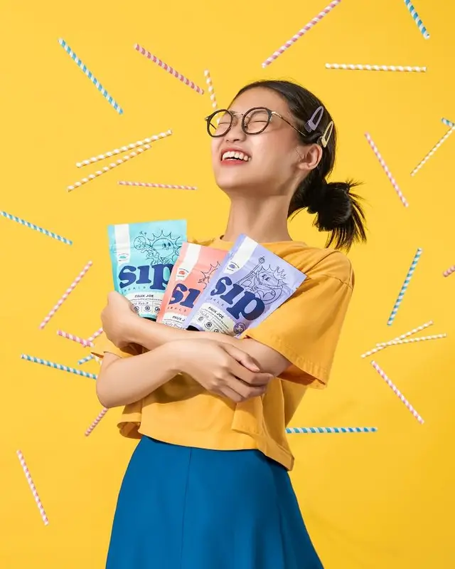 Smiling woman hugging 'sip' drink pouches on yellow background
