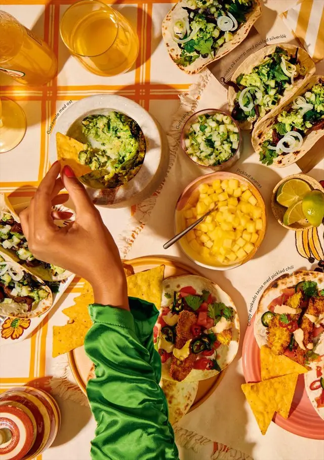 Overhead spread: fish tacos, guacamole and mango salsa on orange plaid tablecloth