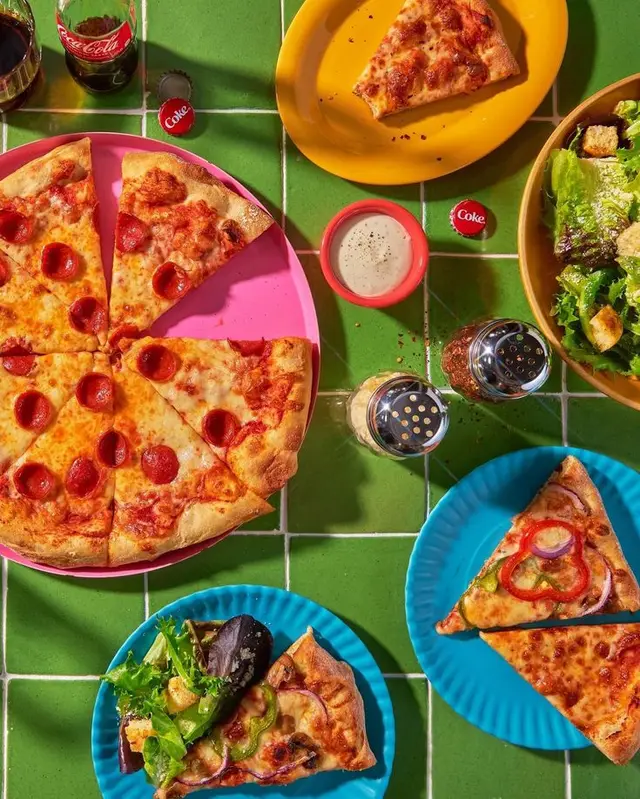 Pepperoni pizza and salads on green tiled table with Coca‑Cola