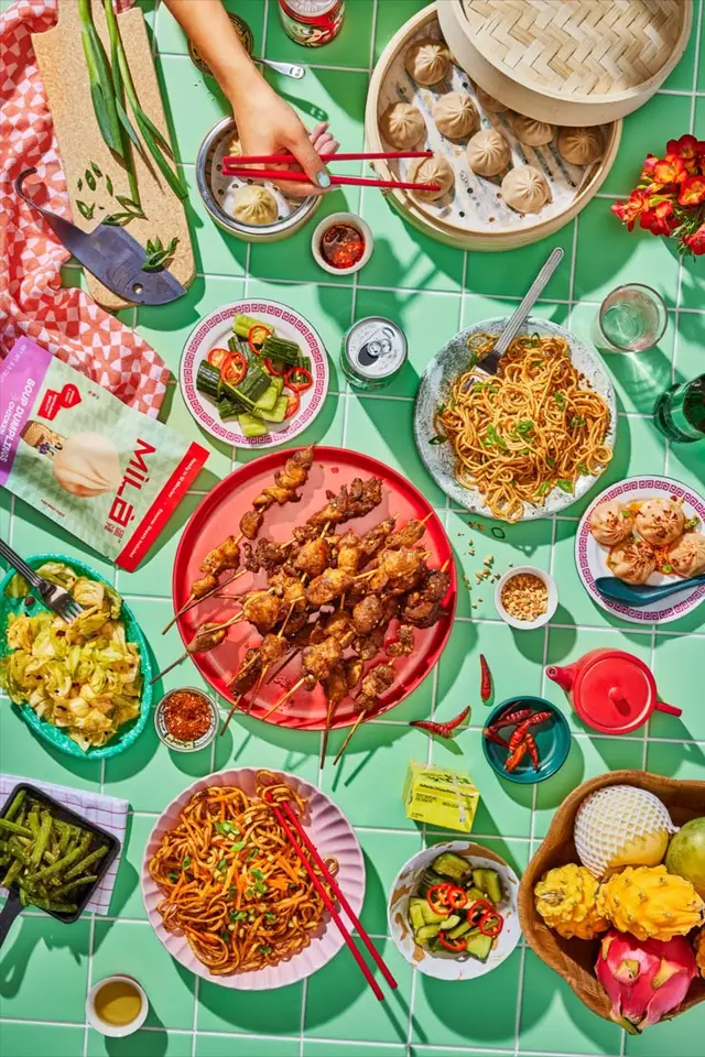 Vibrant Asian picnic flatlay — bamboo steamer, skewers and noodles on mint-tile table