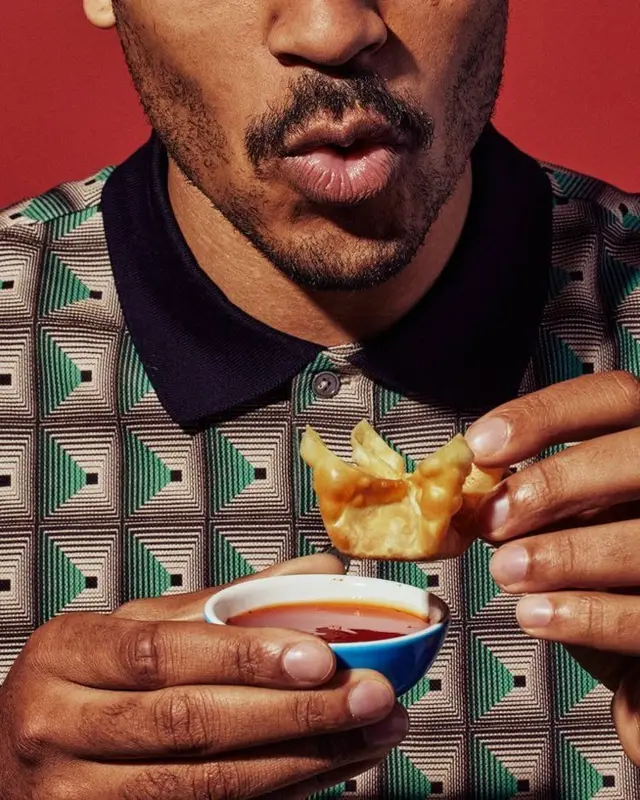 Close-up: hand dipping fried wonton into chili sauce