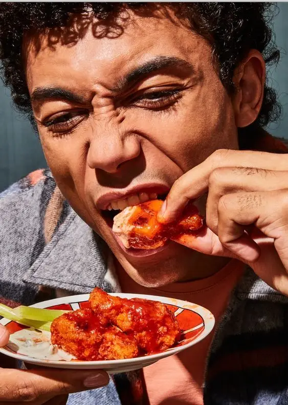 Close-up: person biting buffalo-style sauced chicken bites with celery and dip