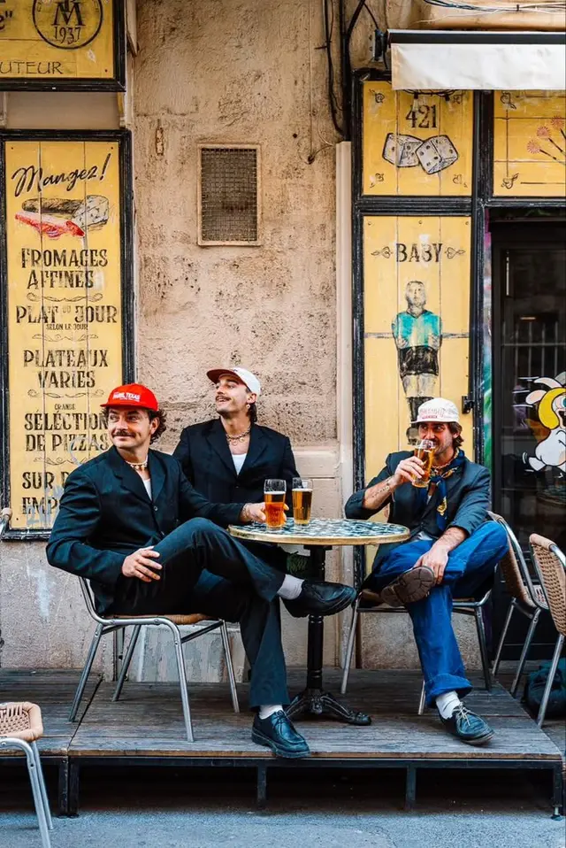 Three men drinking beer at a yellow French-style bistro storefront