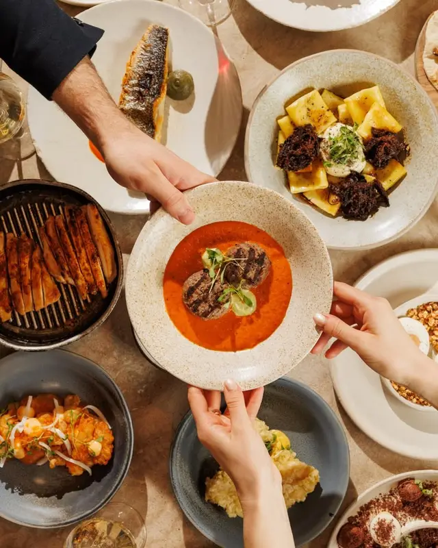 Overhead restaurant spread with tomato-based meat dish and assorted plates