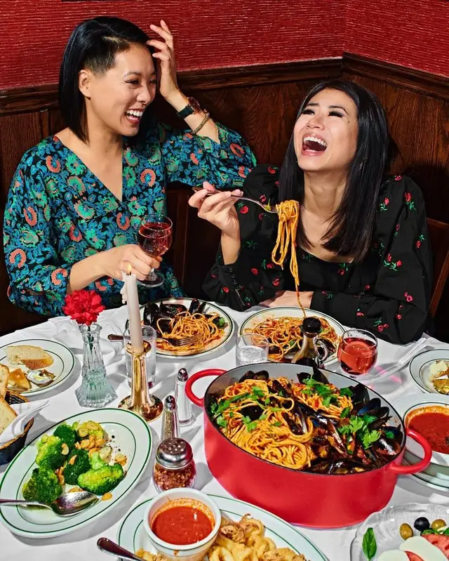 Friends sharing family-style spaghetti and mussels in a red enameled pot, candlelit booth