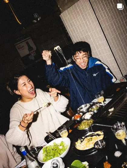 Candid flash photo of two diners laughing over a hot skillet with cheese pull