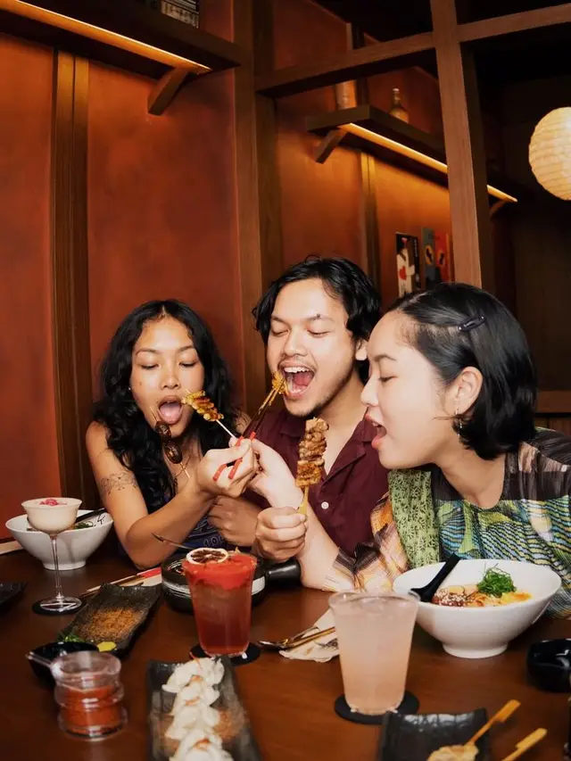 Friends sharing yakitori, ramen and cocktails in a warm wood izakaya