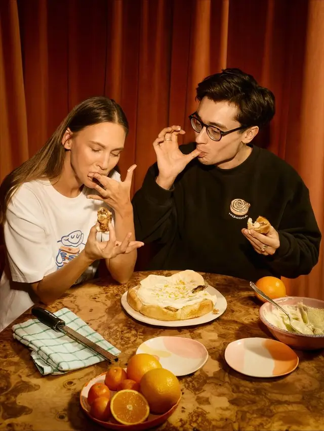 Tasting a cream-topped round pastry at an orange-curtained table
