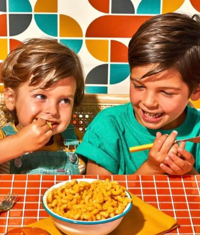 Kids sharing mac and cheese at a retro tiled table