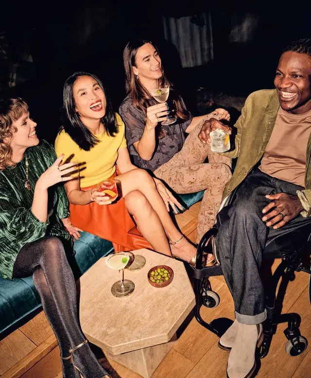 Friends Laughing with Cocktails on Teal Velvet Sofa in Lounge