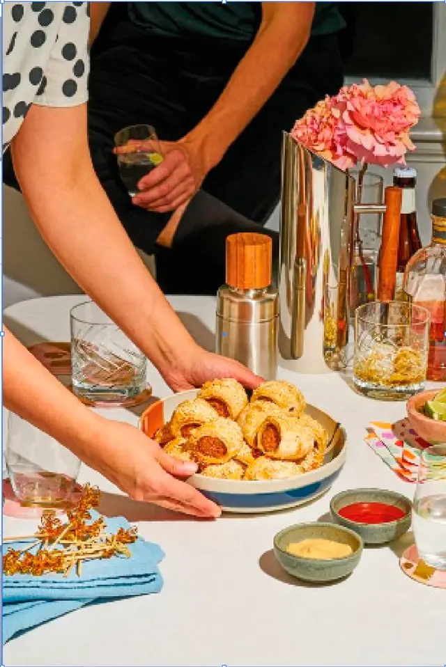 Cocktail table with sausage rolls, whiskey glasses and pink flowers