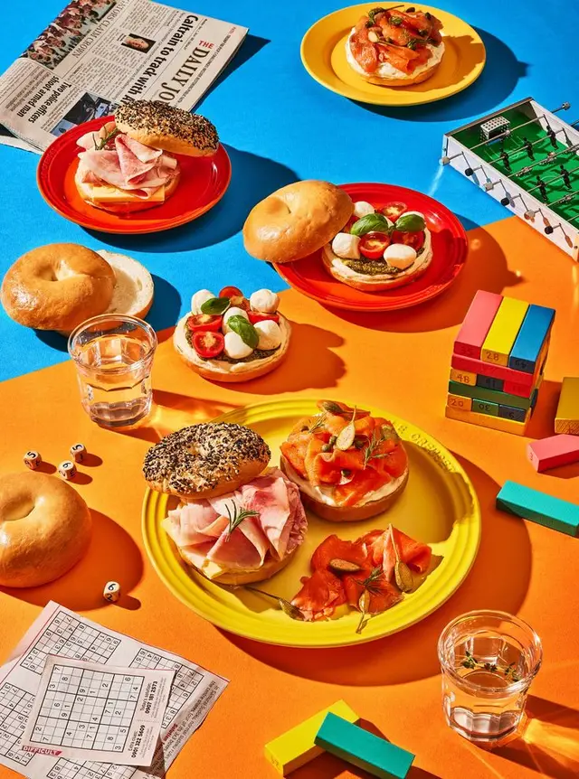 Color-blocked brunch flatlay with bagels, smoked salmon, mozzarella and ham