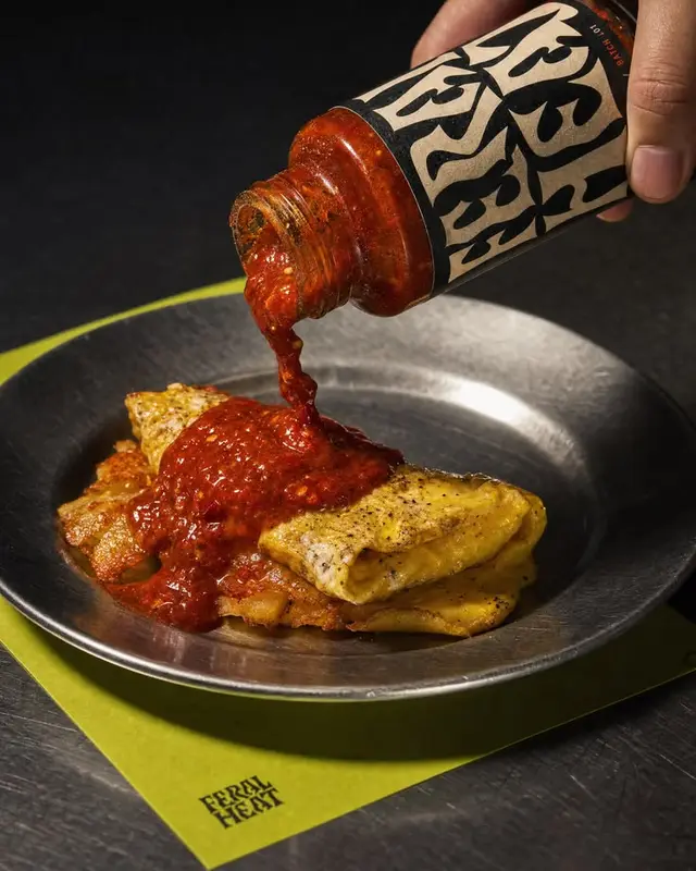 Feral Heat hot sauce poured over folded omelette on metal plate