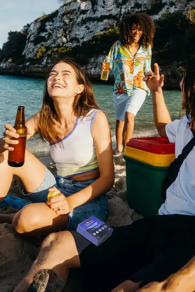 Friends laughing on a sandy beach cove with green cooler and beers
