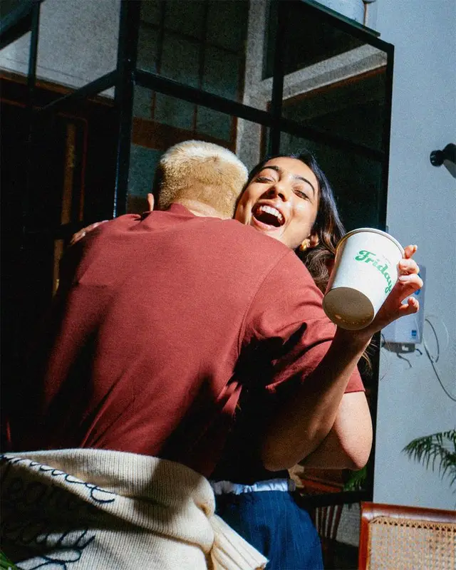Candid hug with white takeaway cup showing green cursive logo