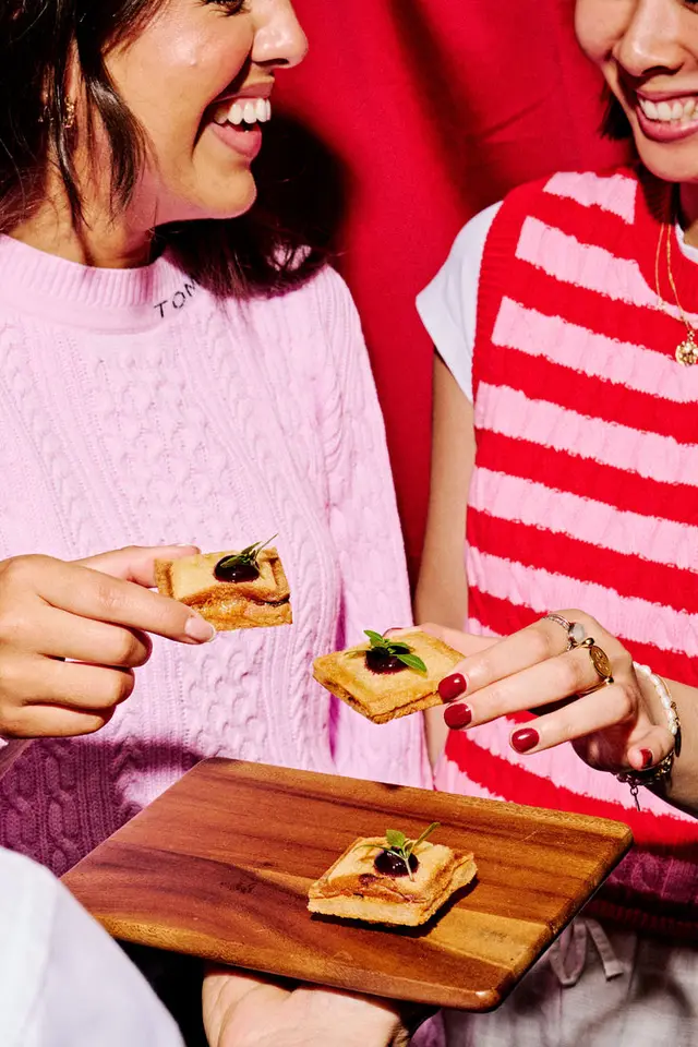 Two people sharing square crostini on a wooden serving board