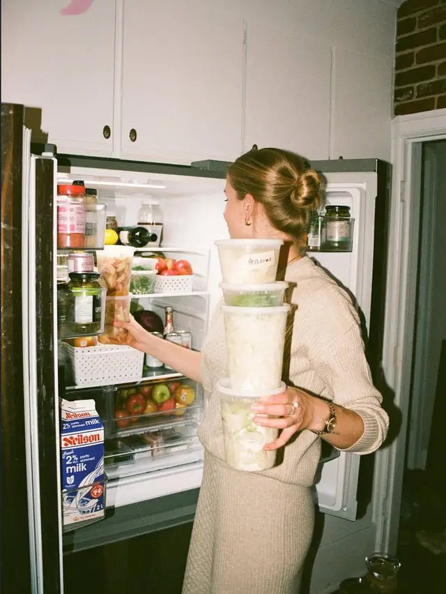 Person stacking meal-prep tubs in open refrigerator (Neilson 2% milk visible)