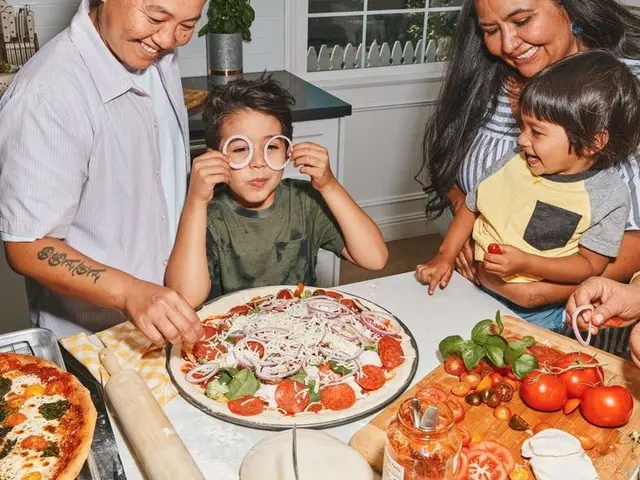 Family assembling homemade pepperoni and red onion pizza on marble countertop