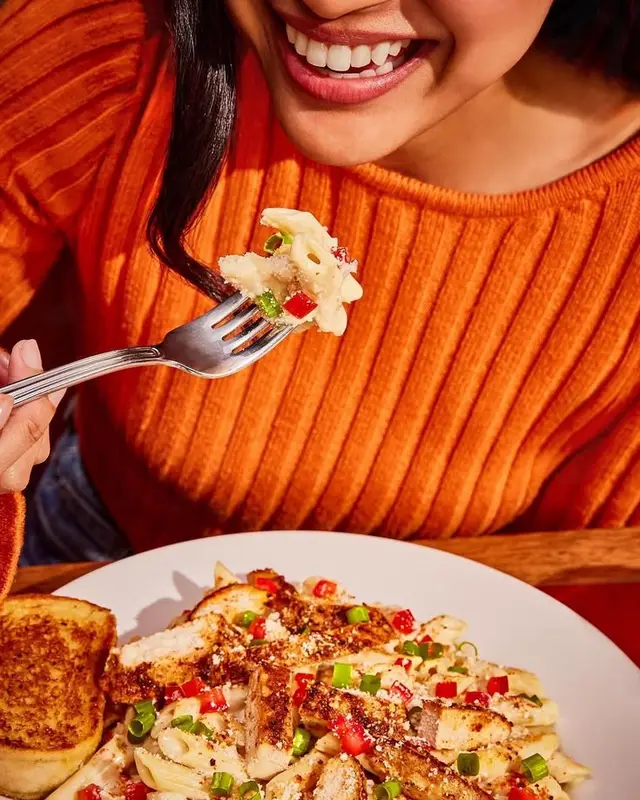 Forkful of cheesy penne with grilled chicken, diced red pepper and scallions