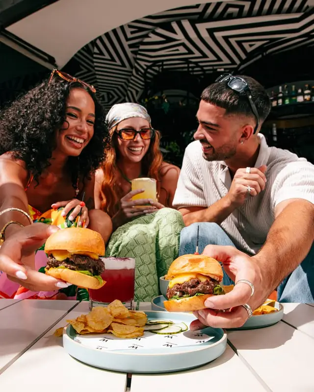 Friends sharing cheeseburgers and cocktails under a black-and-white geometric canopy