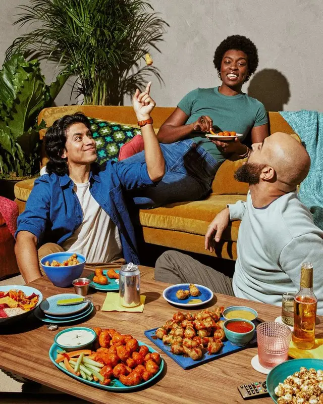 Friends sharing finger-foods on mustard velvet sofa