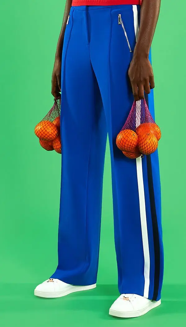 Editorial: Royal blue track pants with oranges in purple mesh bags on green backdrop