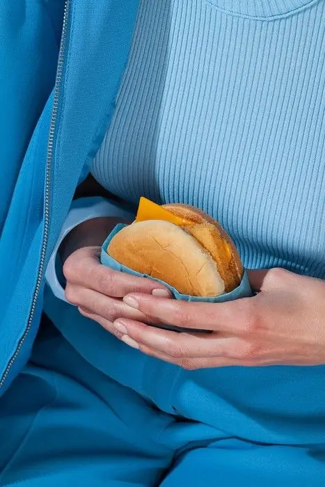 Monochrome blue outfit holding cheeseburger with cheddar slice
