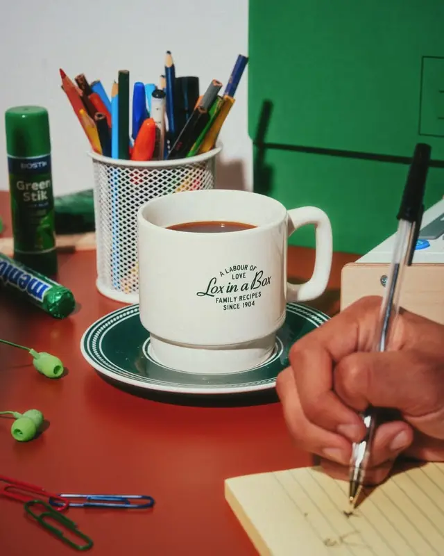 Coffee mug labeled 'Love in a Box' on red desk with stationery