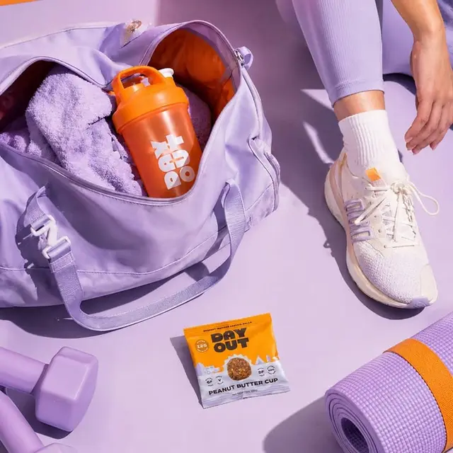 Lavender gym flat-lay with orange shaker and 'DAY OUT' peanut butter cup