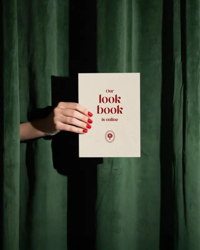 Cream lookbook announcement card held against dark green velvet curtain