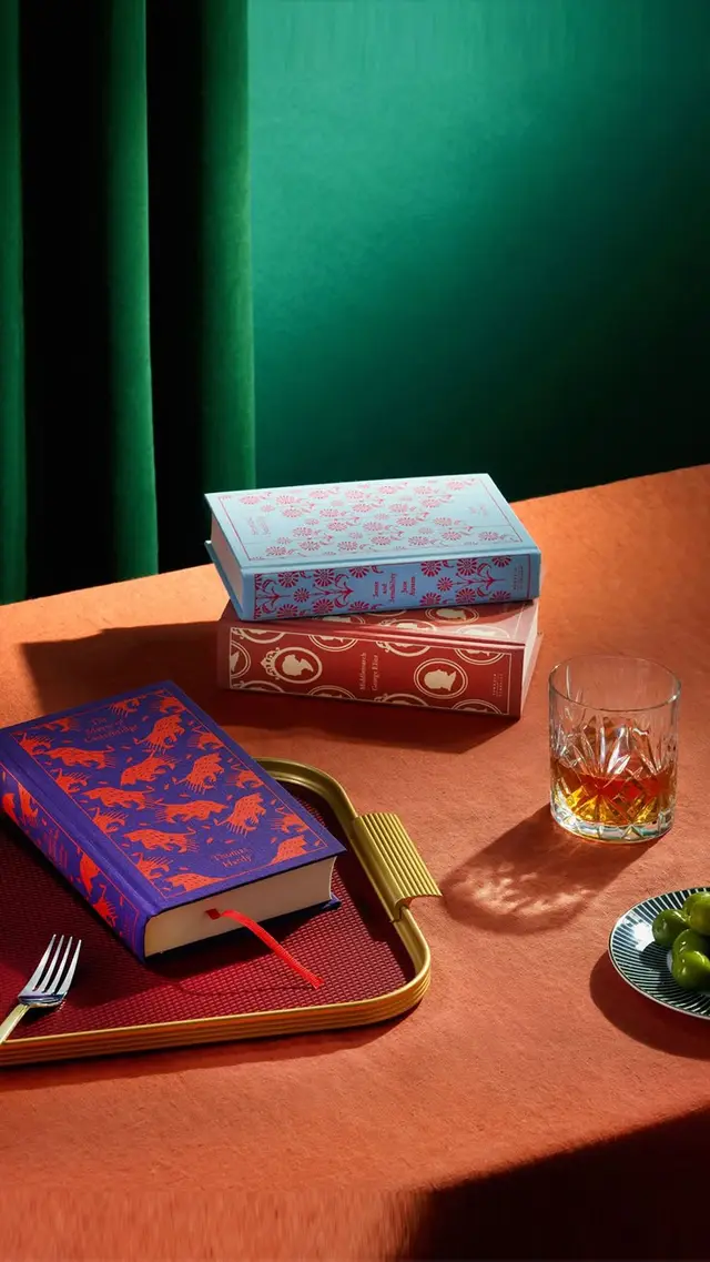 Patterned hardcover books and whiskey glass on terracotta tabletop