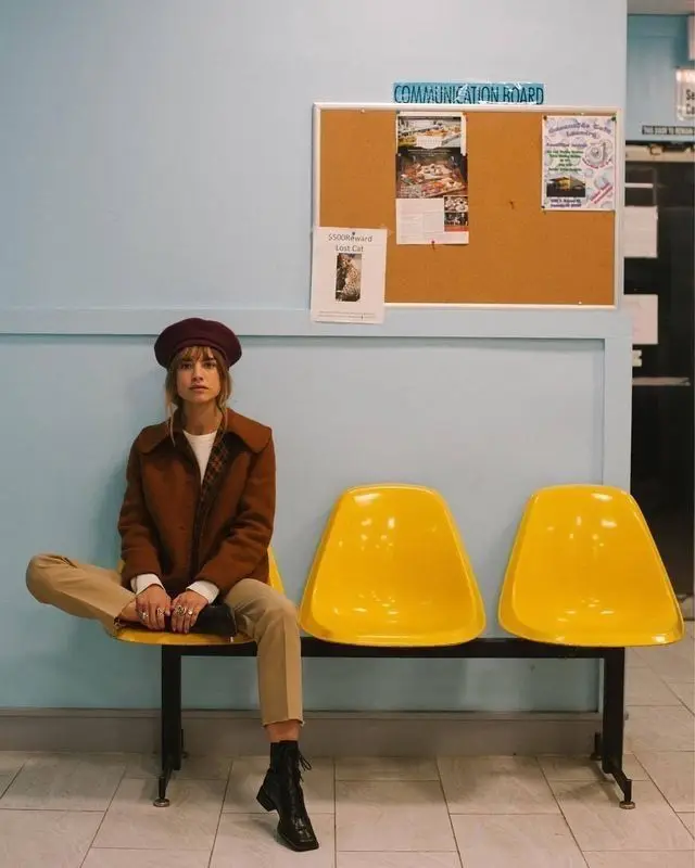 Woman in beret seated on yellow waiting-room chairs