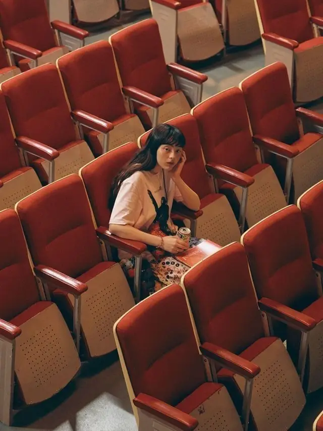 Woman seated alone in empty red theater rows