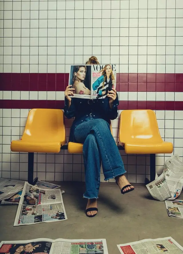 Person reading VOGUE on yellow bench in tiled waiting area